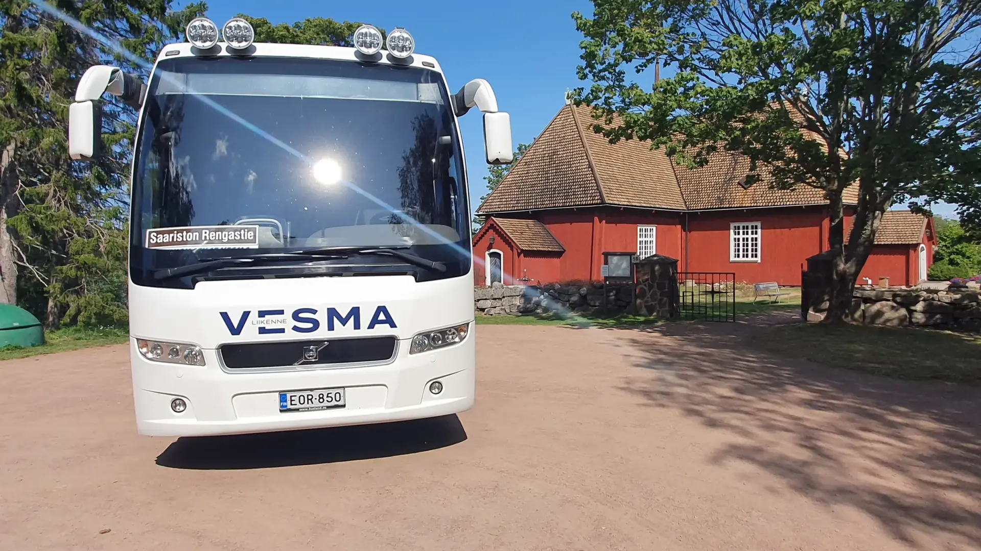Vesman bussi pysäköitynä punaisen puurakennuksen eteen saaristossa