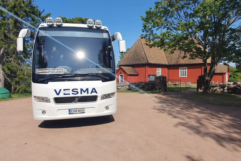 Vesman bussi pysäköitynä punaisen puurakennuksen eteen saaristossa